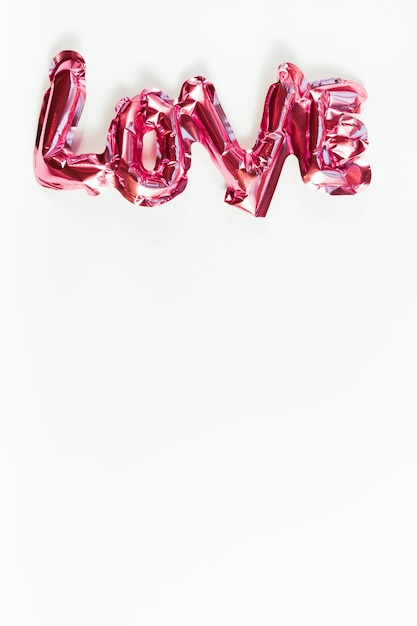 Valentijnsdag creatief concept. Opblaasbare roze glanzende folie ballon woordteken liefde met schaduwen geïsoleerd op een witte achtergrond.