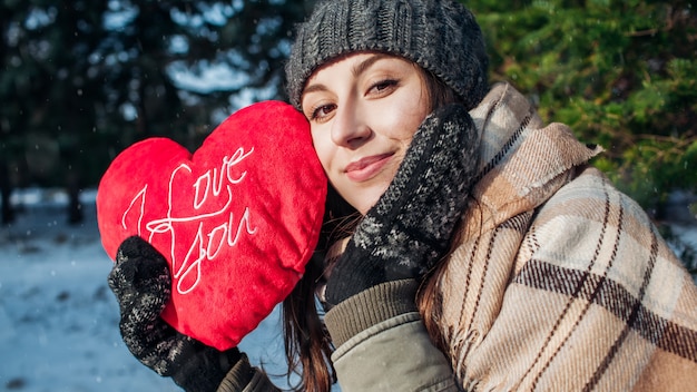 Valentijnsdag. De jonge vrouw houdt rood hoofdkussenhart gevormd met I houdt van u schrijvend in de winterbos