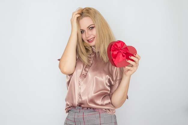 Valentijnsdag - dromende vrouw die in roze blouse het rode hart van de giftdoos houdt