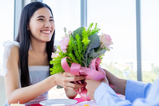 Valentijnsdag en Aziatische Jonge gelukkige paar concept, een man met een boeket rozen geven aan vrouw met handen lachend haar gezicht wacht verrassing na de lunch in een restaurant