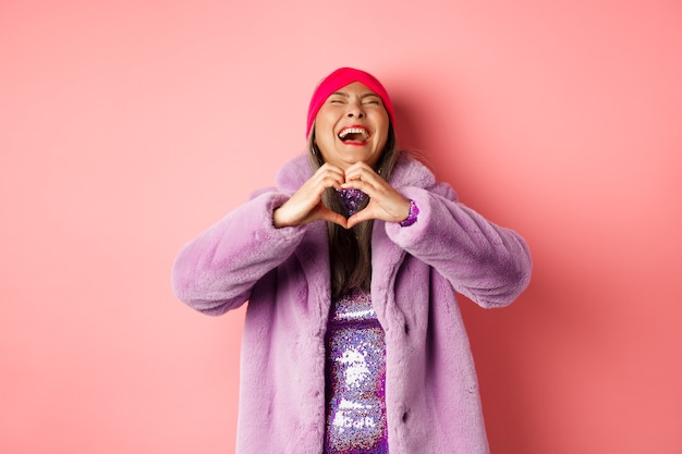 Valentijnsdag en shopping concept. Gelukkige aziatische vrouw in modieuze uitrusting die hartteken tonen en zorgeloos lachen