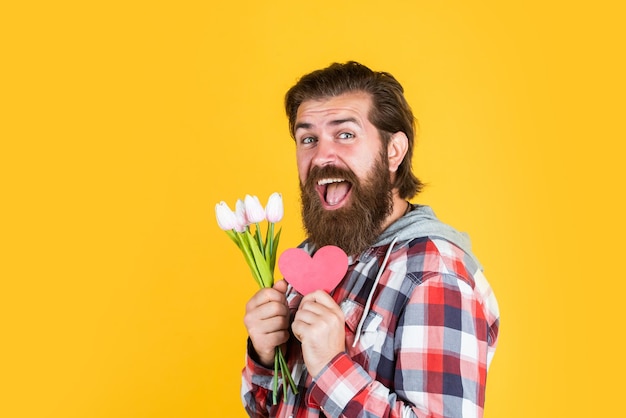 Valentijnsdag feest gelukkige verjaardagscadeau met liefde lente boeket voor haar klaar voor romantische date aanwezig voor dames en moeders dag gelukkige bebaarde man houd tulp bloemen en decoratief hart vast