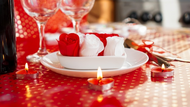 Valentijnsdag. Fles wijnstok, glazen, rode rozen, kaarsen - rode achtergrond. Liefde diner concept