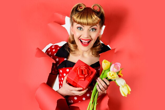 Valentijnsdag. Gelukkige vrouw die met gift en bloem door document kijkt. Pin-up girl met cadeau.