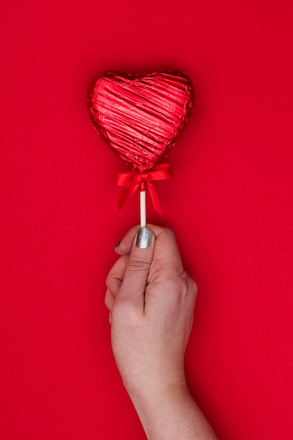 Valentijnsdag geschenk Vrouwelijke hand met een hartvormige lolly tegen een rode achtergrond