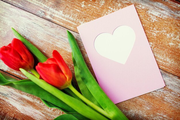 Valentijnsdag, groet, liefde en vakantie concept - close-up van rode tulpen en wenskaart met hart