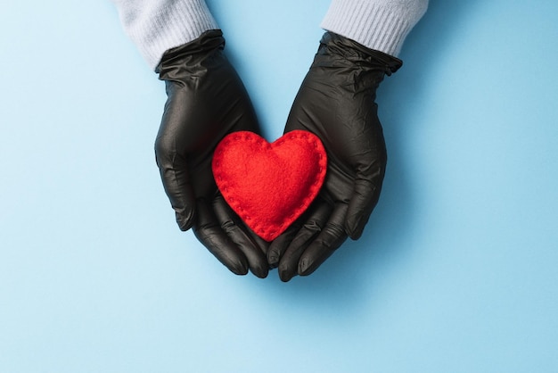 Valentijnsdag in 2021 tijdens de Covid-19-pandemie en de coronavirusziekte. Rood hart op de handpalmen van een vrouw beschermd door medische handschoenen