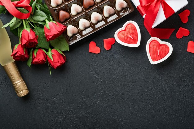 Valentijnsdag kaart Rose rode bloemen brownie koekjes en chocoladesuikergoed op hartvormige geschenkdoos met wijn op zwarte achtergrond Moederdag of Vrouwendag wenskaart Bovenaanzicht plat leggen