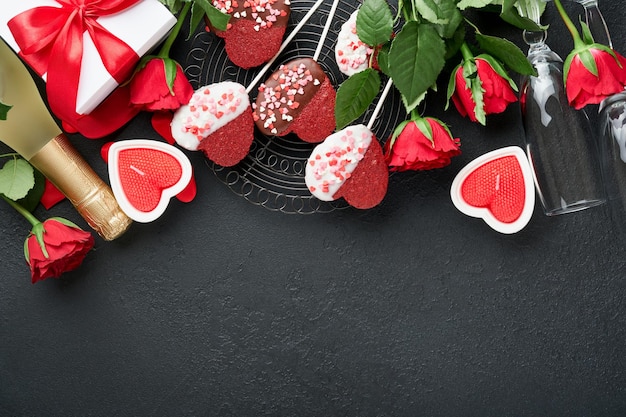 Valentijnsdag kaart Rose rode bloemen brownie koekjes en chocoladesuikergoed op hartvormige geschenkdoos met wijn op zwarte achtergrond Moederdag of Vrouwendag wenskaart Bovenaanzicht plat leggen