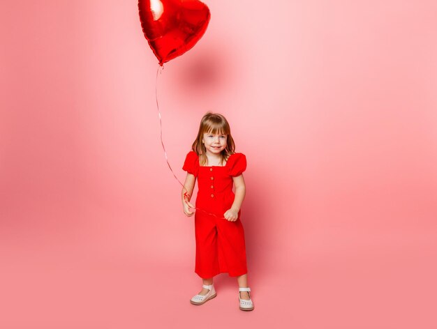 Valentijnsdag, klein meisje met een grote ballon in de vorm van een hart op een roze achtergrond.