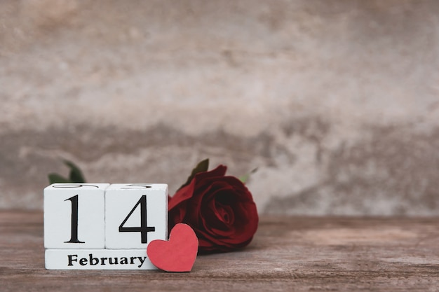 Valentijnsdag met 14 februari. Houten witte blokkalender, Rode roos en Rood hart op houten lijstachtergrond met exemplaarruimte