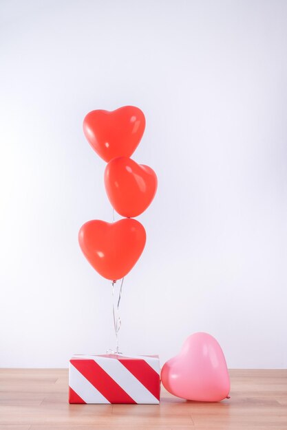 Valentijnsdag, moederdag, verjaardag ontwerpconcept - hart helium ballon met geschenkdoos op een lichte houten vloer, witte muur achtergrond, close-up.