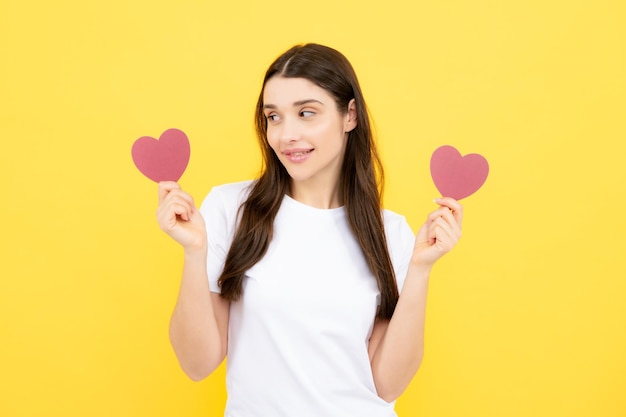 Valentijnsdag Mooie jonge vrouw met hart in haar handen Aantrekkelijke vrouw met papieren hart op gele achtergrond