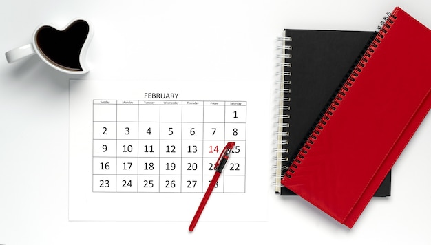 Valentijnsdag op kantoor. februari kalender met kopje koffie hartvorm en gekleurde blocnotes op tafel