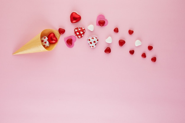 Valentijnsdag plat met snoep hartjes vliegen uit een ijshoorntje op roze