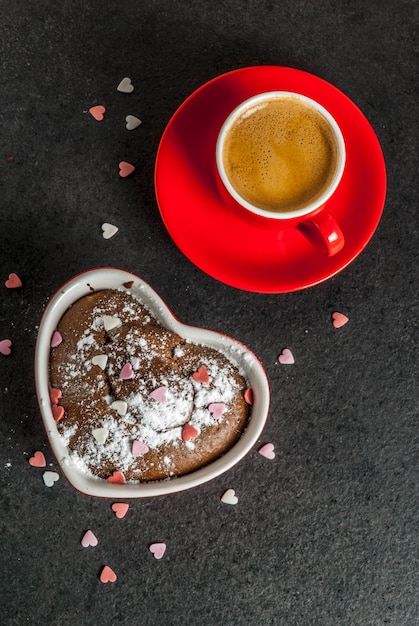 Valentijnsdag, rode koffie mok en chocolade mok cake of brownie met poedersuiker en zoete hartvormige hagelslag, zwart, copyspace bovenaanzicht