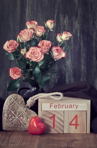 Valentijnsdag stilleven met houten kalender, roze rozen en harten op donker