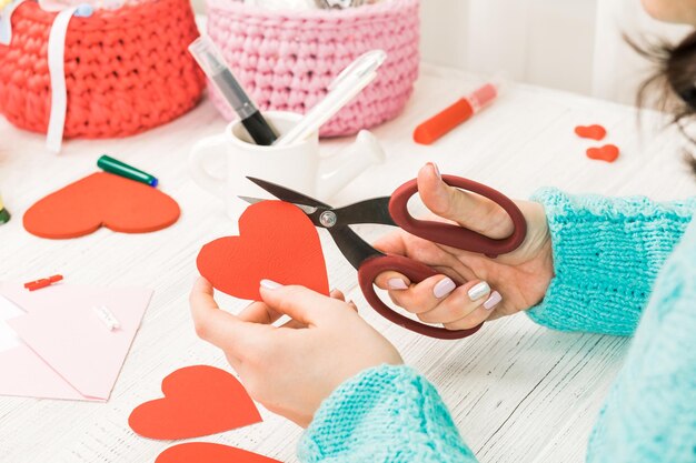 Valentijnsdag thema vrouwelijke handen snijden het hart uit het papier verpakte geschenken tools op een gehavende houten tafel werkplek voor de voorbereiding van handgemaakte ornamenten