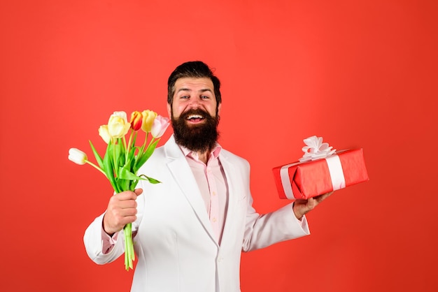 Valentijnsdag vrouwen dag verjaardag knappe man houdt geschenkdoos en bloemen zakenman met cadeau en
