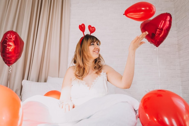 Valentijnsdag, Vrouwendag. Jong kaukasisch meisje dat in bed zit en valentijnsdag viert met een hartvormige ballon in haar handen