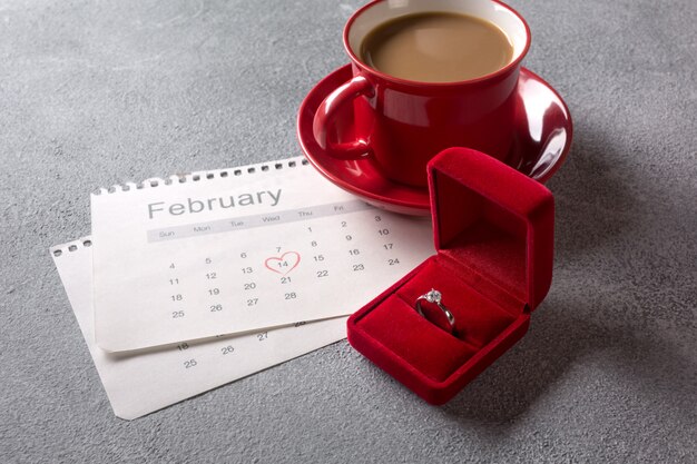 Valentijnsdag wenskaart. Rode koffiekop, ring en geschenkdoos over februari kalender.