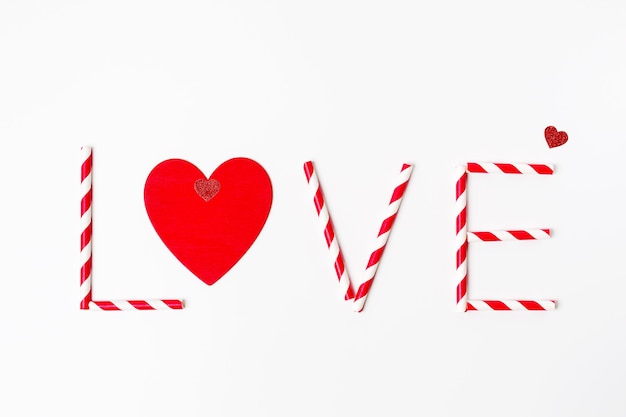 Valentijnsdag wenskaart, tekst Love gemaakt van gestreepte rode en witte rietjes en rood hart op witte achtergrond