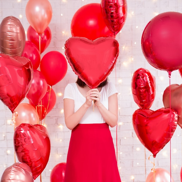 Valentijnsdagconcept - slanke vrouw die haar gezicht bedekt met hartvormige ballon