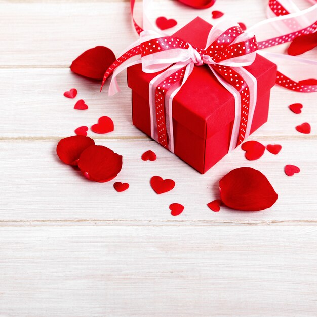 Valentine background of gift box and rose petals on white wood