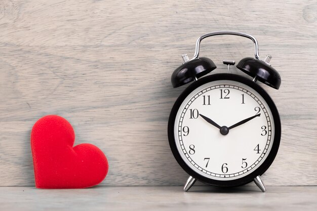 valentine concept. alarm clock with red heart on wooden background close up