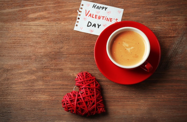 赤いハートと木製のテーブルの背景にメモとコーヒーのバレンタインコンセプトカップ