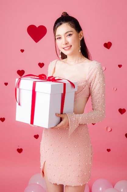 Valentine concept Young Asian sexy woman gathered in ponytail with natural makeup on face have plump lips and clean fresh skin holding gift box with balloon on pink heart pattern background