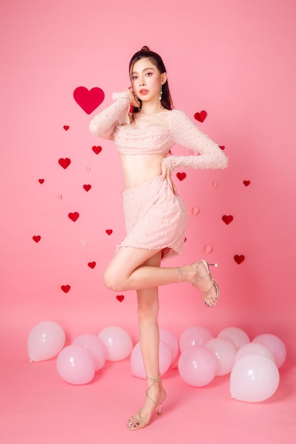 Valentine concept young asian sexy woman gathered in ponytail with natural makeup on face have plump lips and clean fresh skin slim fit body standing with balloon on pink heart pattern background