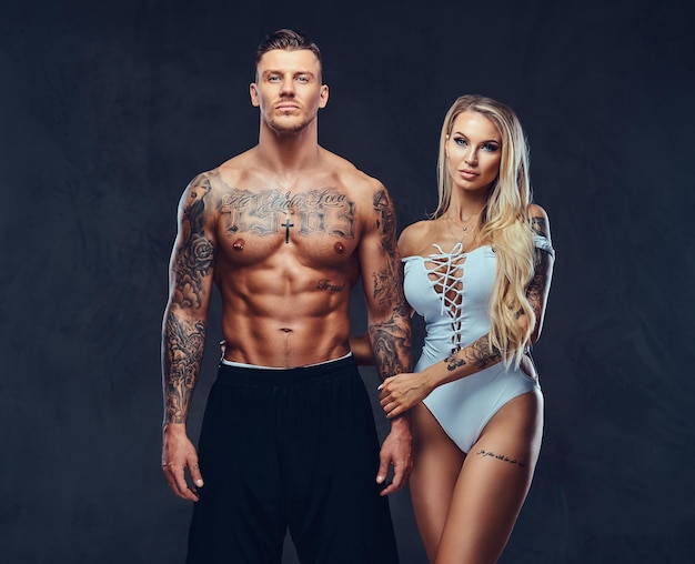 Valentine couple, handsome tattooed male and alluring girl holding hands, posing in studio.