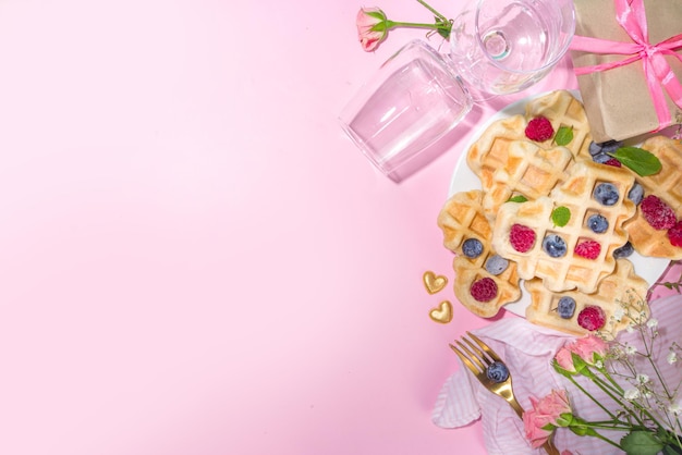 Valentine day brunch menu background with various breakfast and lunch dishes, waffle, croissant, muffins, donuts, berries, fries scrambled eggs, pancakes, pink background copy space