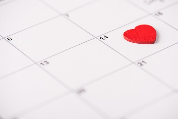 Valentine day celebration concept. Close up view photo of calendar with lying on it red heart on 14th february