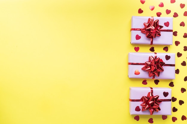 Композиция дня валентинки, поздравительная подарочная коробка с сердечками конфетти на желтом фоне. Плоская планировка.