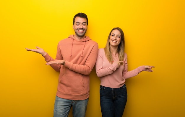 In valentine day Group of two people on yellow background holding copyspace imaginary on the palm to insert an ad