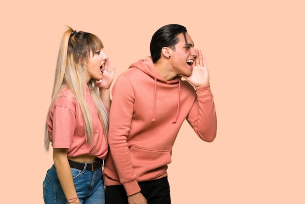 In valentine day Young couple shouting with mouth wide open to the lateral over pink background