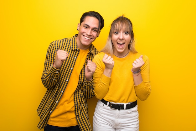 In valentine day Young couple over vibrant yellow background celebrating a victory in winner position