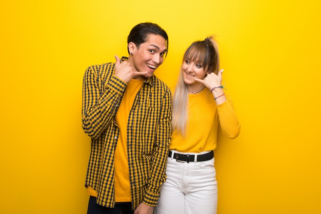 In valentine day Young couple over vibrant yellow background making phone gesture. Call me back sign