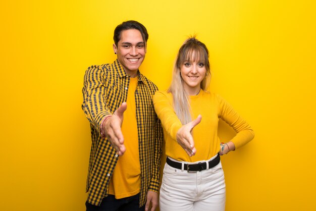 In valentine day Young couple over vibrant yellow background shaking hands for closing a good deal