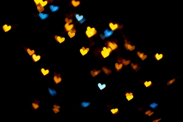 バレンタイングランジハート型ライトの背景。黒の背景に黄色の金と青のハート型の装飾のためのカラフルな照明ボケバレンタイン、愛の写真の背景