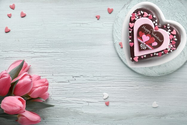 Valentine hart cake met chocolade, suiker decoraties en tekst "Happy Valeitine" en roze tulpen,