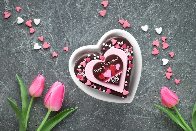 Valentine heart cake with chocolate and sugar decorations and greeting text "Happy Valeitine" and pink tulips