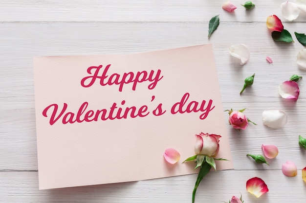 발렌타인 데이, 핑크 장미 꽃과 꽃잎이 흰색 소박한 나무에 흩어져 있고 인사말 카드가 열립니다.