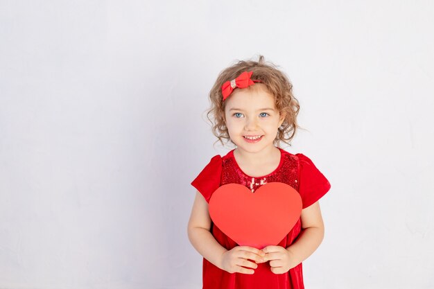 Foto bambino di san valentino. bambina in vestito rosso che tiene grande cuore