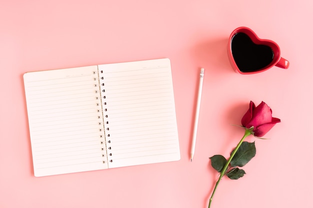 Sfondo di san valentino. tazza di caffè nero, rosa rossa e taccuino su rosa pastello a forma di cuore