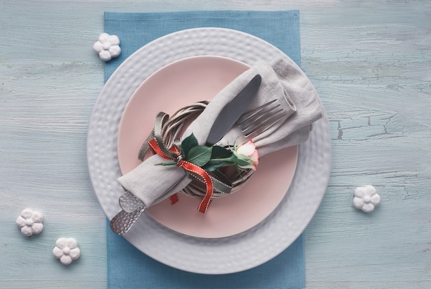 발렌타인 데이, 생일 또는 기념일 테이블 설정, 밝은 질감 배경에 상위 뷰. 장미 꽃 봉오리와 리본, 세라믹 꽃과 분홍색 장미로 장식 된 냅킨과 그릇