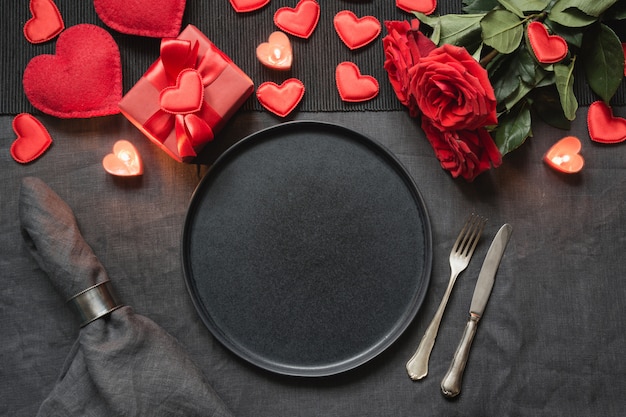 Valentine's day or birthday dinner. Romantic table setting with red rose on black linen tablecloth.