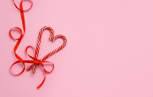 ピンクの背景に赤いリボンとバレンタインデーのキャンディロリポップハートの形、。